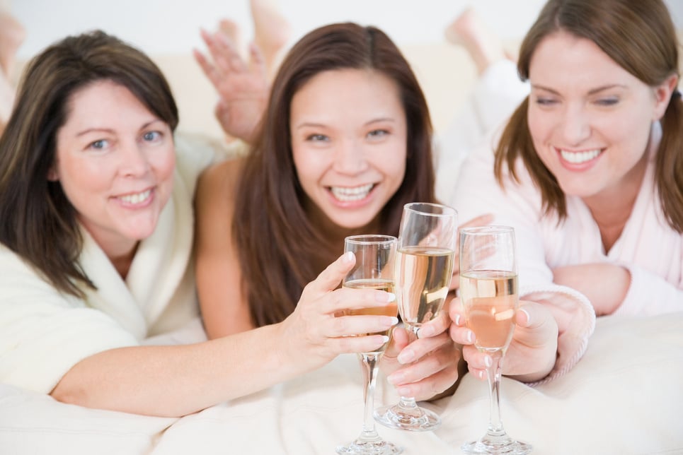 Three women on bed toasting champagne